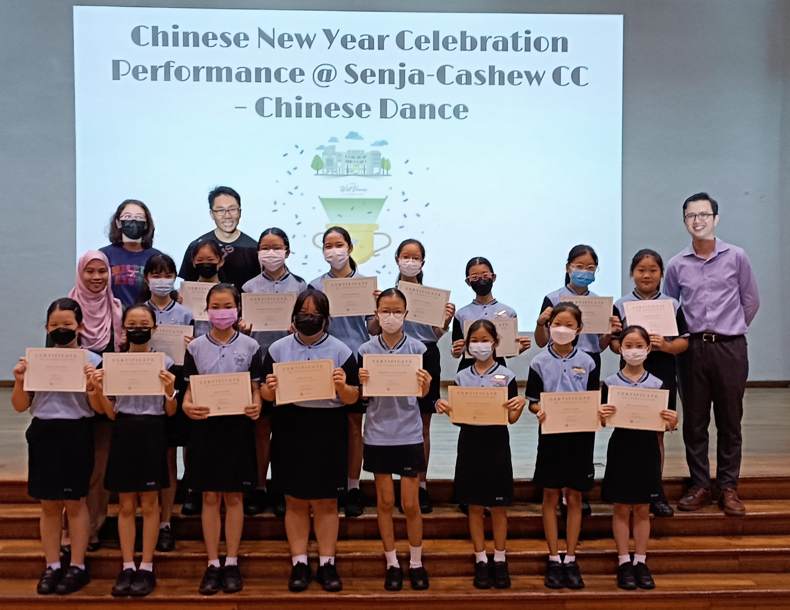 Students in uniform hold certificates on a stage in front of a Chinese New Year Celebration Chinese Dance slideshow.